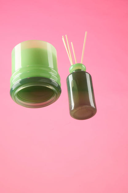 The Minty Verde - Stack 3.2 oz Diffuser, featuring a green jar lid and vessel with reed sticks, stands out against a bold pink background, offering lasting freshness.