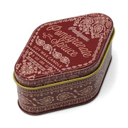Decorative maroon tin in a rounded triangle shape featuring ornate cream lettering and floral patterns on the lid, labeled “Pomegranate Spruce - Station 3.5 oz Tin Candle,” inspired by the woody scents of Northern California.