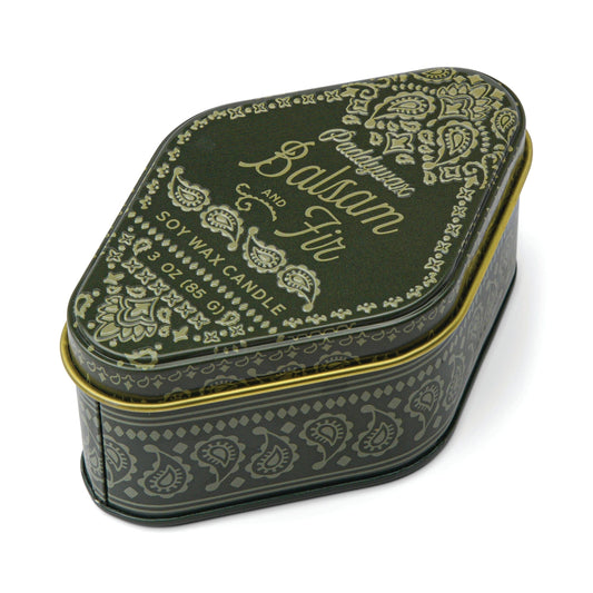 Dark green, paisley-patterned tin with gold decorative accents and text reading "Balsam & Fir - Station 3.5 oz Tin Candle" on the lid. This travel-sized, rounded triangle tin is perfect for adventures and captures woody aromas evoking lush forests.