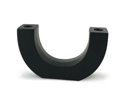 Introducing the U Taper Holder - Black: a sleek, U-shaped ceramic piece with flat sides and two small holes on top, designed to stand upright against a white background. Ideal as minimalist decor or as an eye-catching black candle holder, the U Taper Holder - Black artfully combines form and function.