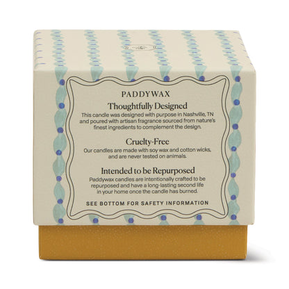 The Wisteria & Willow - Tulip 5.5 oz Candle features a teal glass vessel with blue and yellow patterns. The label states: Paddywax, Thoughtfully Designed, Cruelty-Free, Intended to be Repurposed, with ethical and sustainable production.