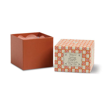 An orange box with its lid removed sits beside the patterned 'Cactus Flower - Tulip 5.5 oz Candle' lid, revealing pink contents—adding a charming touch to your decor and reminiscent of a stylish candle display.