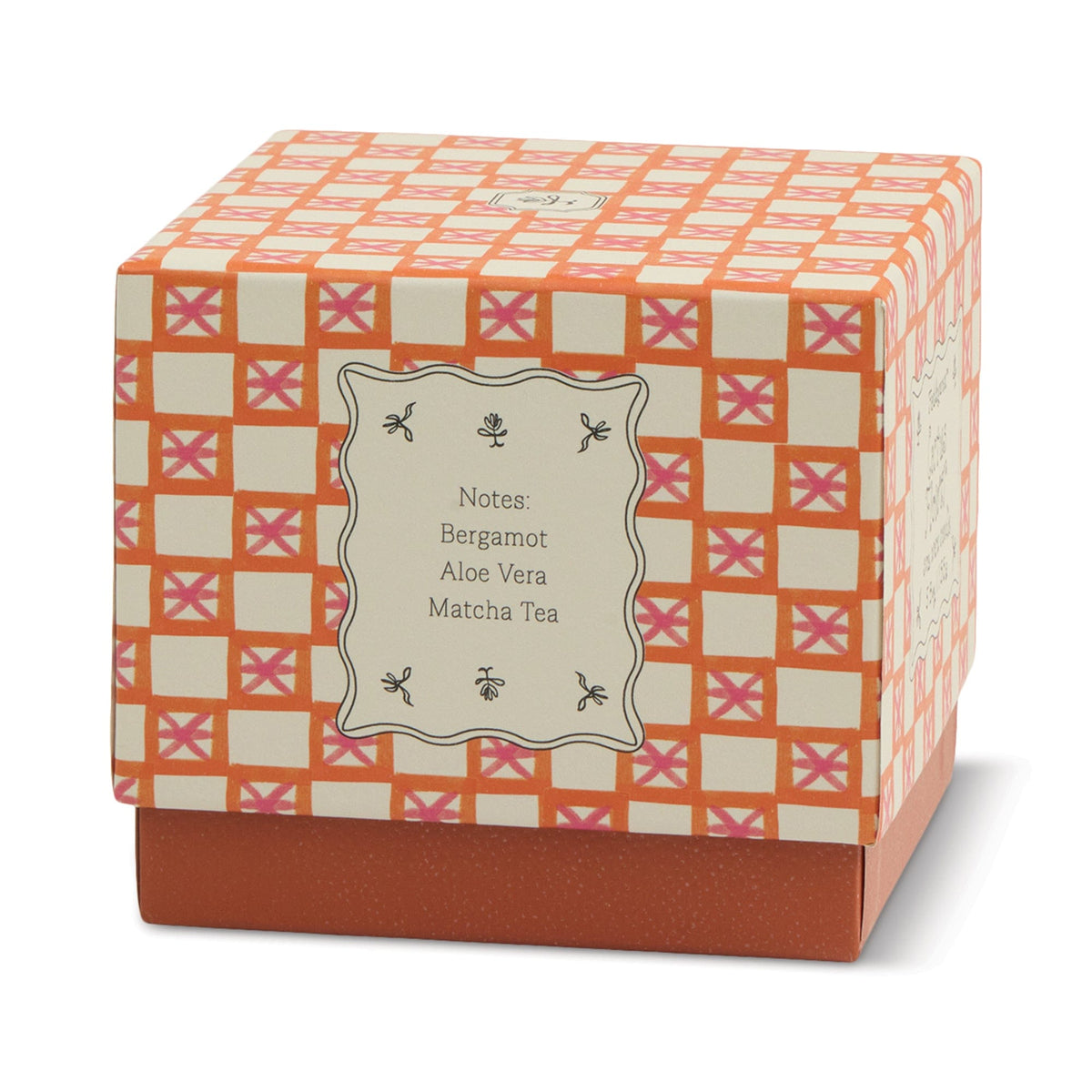 A decorative box with an orange, pink, and cream checkered pattern and a script label detailing notes of Bergamot, Aloe Vera, Matcha Tea—perfect to pair with your favorite Cactus Flower - Tulip 5.5 oz Candle for a stylish touch of home decor.