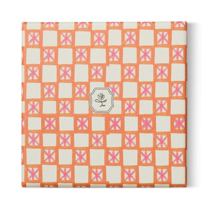 A square package with an orange and pink checkered design and a central white label with a black flower—ideal for gifting the Cactus Flower - Tulip 5.5 oz Candle or enhancing your home decor.