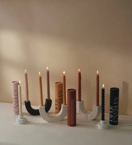 A row of lit, sleek Burnt Orange & Peach Tube Tapers (set of 4) in modern holders, with their cylindrical packaging behind—an elegant choice for sophisticated dining settings.
