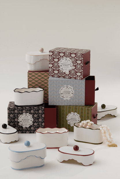 A cluster of ornate boxes sits beside Lavender & Thyme - Chérie 5.5 oz Ceramic Candle, a porcelain vessel holding a pearl necklace and hinting at delicate fragrance notes in the air.