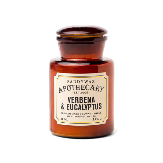 A brown amber glass apothecary jar candle labeled "Verbena + Eucalyptus - Apothecary 8 oz Candle," hand-poured in the USA with artisan soy wax and a vintage-inspired fragrance.