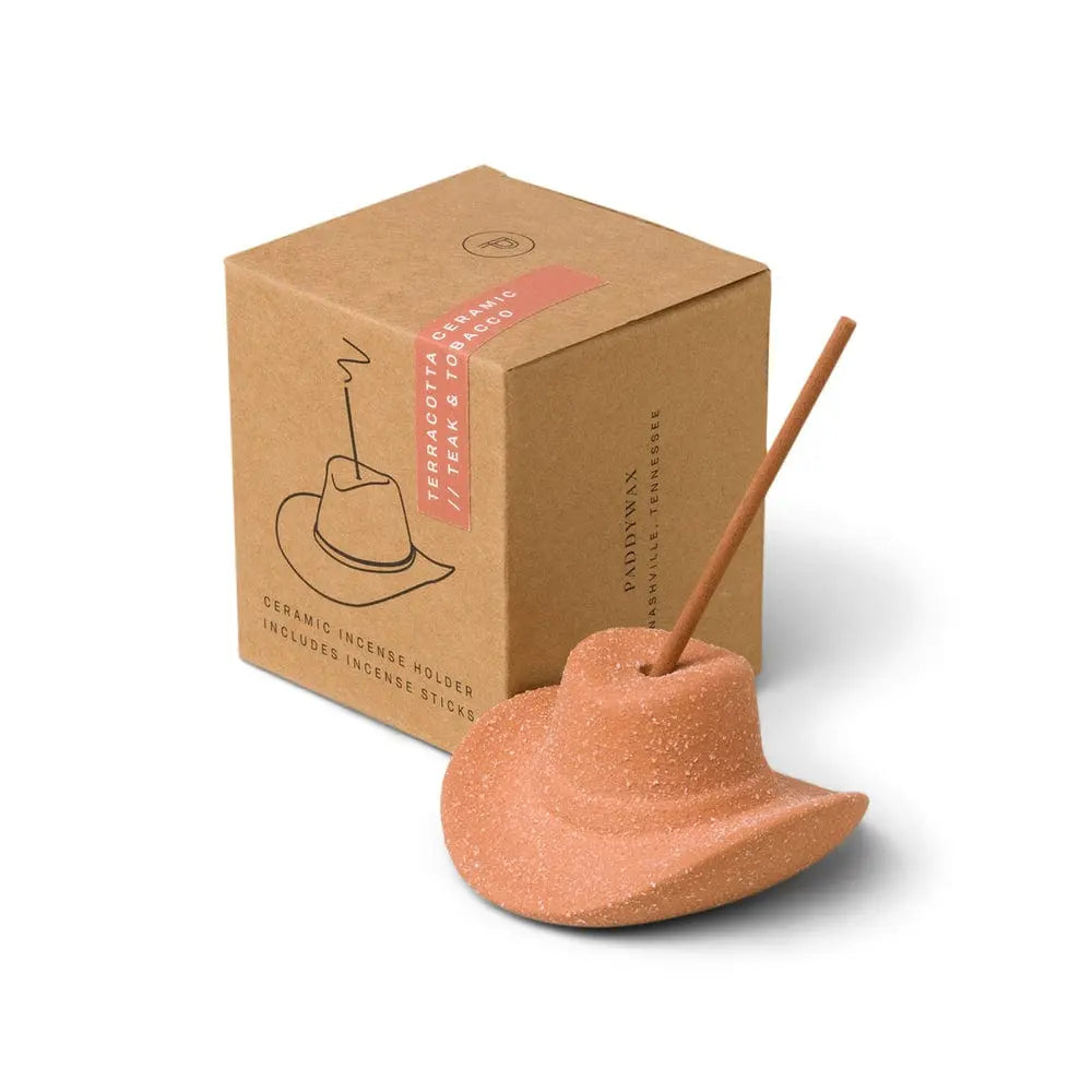 The Teak & Tobacco - Incense Holder features a cowboy hat design with a teakwood tobacco incense stick, displayed beside its brown cardboard packaging.