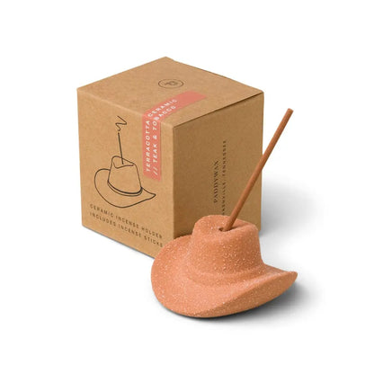 The Teak & Tobacco - Incense Holder features a cowboy hat design with a teakwood tobacco incense stick, displayed beside its brown cardboard packaging.
