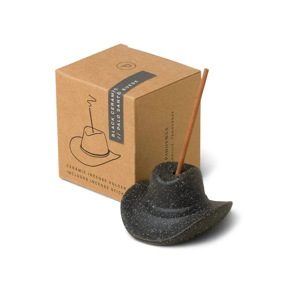 The Palo Santo Suede - Incense Holder is a black ceramic cowboy hat with an incense stick, shown next to its brown box—ideal for Nashville-inspired decor.