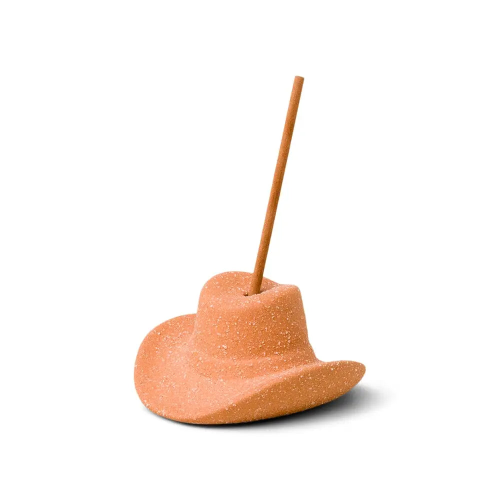 A Teak & Tobacco - Incense Holder, made of textured clay-like material and shaped like a cowboy hat, holds a brown incense stick and is displayed against a plain white background.