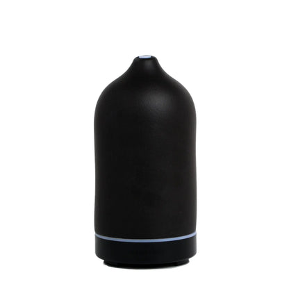 The Electronic Oil Diffuser - Black is a matte black, cylindrical ceramic diffuser with a rounded top and a small opening, designed for aromatherapy, shown sitting on a flat white surface.