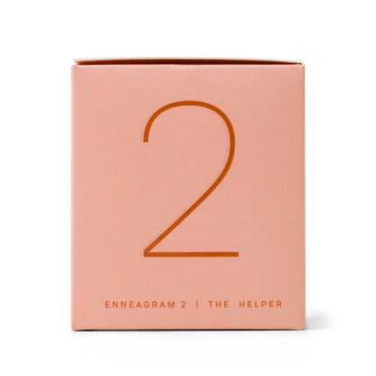 A pink box displaying a large number 2 on the front, with "ENNEAGRAM 2 | THE HELPER" printed below in small capital letters. The Enneagram #2 Helper 5 oz Candle - Violet + Vanilla comes in ombre glass and makes a thoughtful and stylish gift, perfect for adding a personal touch to any space.