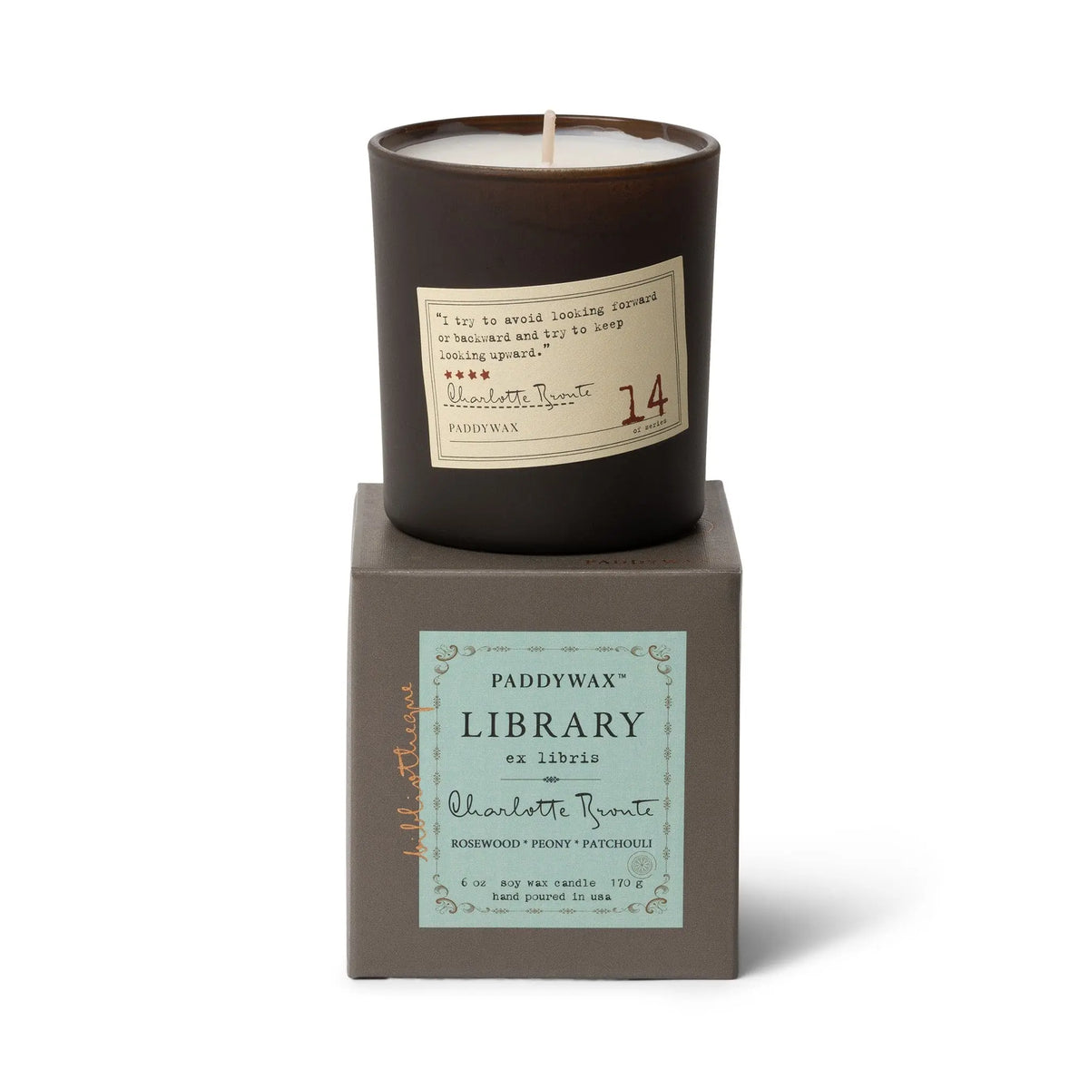 The Charlotte Bronte - Library Candle 6 oz, a dark brown literary candle in a glass jar with rosewood, peony, and patchouli notes, sits atop a gray Paddywax Library Collection box—an ideal fragrance gift for book lovers.