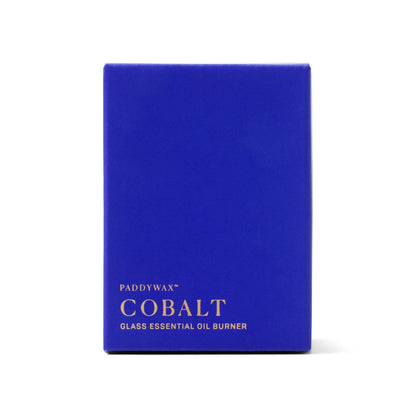 A cobalt blue rectangular box with gold text reads "Cobalt Blue Glass - Essential Oil Burner & Tea Light Candle" on the front, perfect for aromatherapy. The box stands upright against a white background.