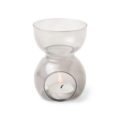 Introducing the Black Glass - Essential Oil Burner & Tea Light Candle, a stylish oil burner made from elegant black glass with a round bowl on top and a tea light candle gently illuminating its base compartment.