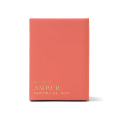 A coral-colored rectangular box with gold text displays "Amber Glass - Essential Oil Burner & Tea Light Candle" on the front. Designed for use with a tea light candle, this essential oil burner features sleek amber glass. The background is white.