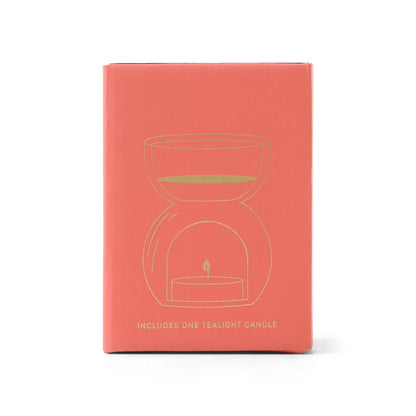 Amber Glass - Essential Oil Burner & Tea Light Candle comes in a coral-colored box featuring a gold line drawing of a tea light candle holder and the message “Includes one tealight candle” on the front—ideal for pairing with amber glass decor or as an essential oil burner.