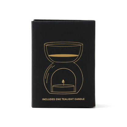 A black box featuring a gold line illustration of the Black Glass - Essential Oil Burner & Tea Light Candle. The text at the bottom reads, Includes one tealight candle.