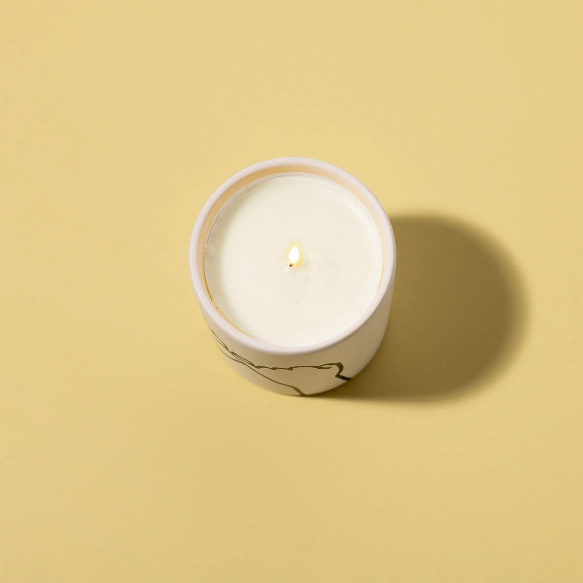 The Wild Fig + Cedar "Pinky Promise" - Impressions 5.75 oz Candle is lit in a round container on a plain beige background, casting a shadow to the right.