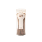 A clear cylindrical container holds brown incense sticks labeled “Cotton + Teak - Haze Incense.” The white label with brown text indicates there are 100 incense sticks inside, making it a perfect addition to any incense collection.
