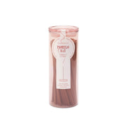 A clear cylindrical holder with a pink lid contains pink Pomelo Bay - Haze Incense sticks. The label highlights the flameless fragrance and states it holds 100 sticks from the incense collection.