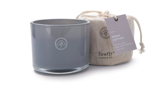 A gray glass “Fresh Cotton - Kindred 10 oz Candle” sits beside a linen bag with a tag reading “Fresh Cotton Soy Wax Candle,” making this candle set perfect for gifting or cozy evenings at home.
