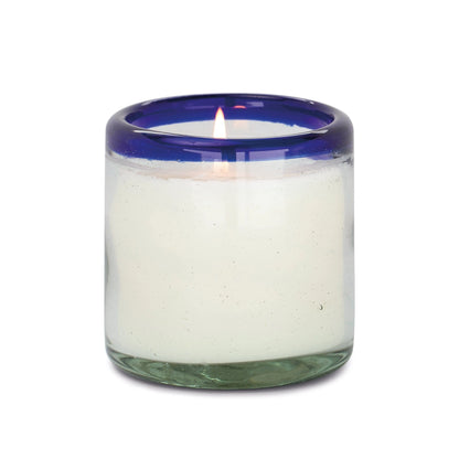 The Salted Blue Agave - La Playa 9 oz Candle is a lit white candle in a clear, hand-blown bubble glass holder with a thick blue rim.