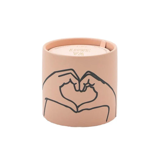 The Tobacco + Vanilla "Love Ya" - Impressions 5.75 oz Candle features a beige ceramic container with a minimalist line drawing of two hands forming a heart on its exterior.