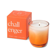 A lit Enneagram #8 Challenger 5 oz Candle—featuring an orange ombre glass holder with a minimalist label—sits beside its matching orange box. The simple, modern design and Incense + Smoke scent make this distinctive Enneagram candle the perfect choice for those wanting a candle with unique personality.