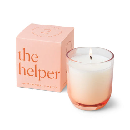 A glowing white Enneagram #2 Helper 5 oz Candle – Violet + Vanilla, in a pink ombre glass holder, sits beside its matching pink box featuring product details on the front—an ideal addition to any Enneagram candles collection or a thoughtful fragrance gift set.